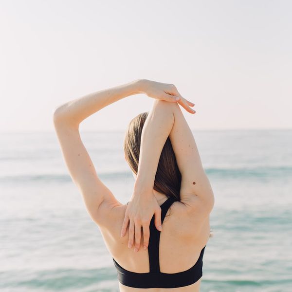 A person stretching gently outdoors, surrounded by nature and morning light.